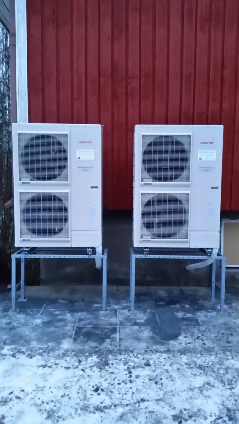 Kaksi ilma-vesilämpöpumpun ulkoyksikköä rinnakkain jalustoilla talvella