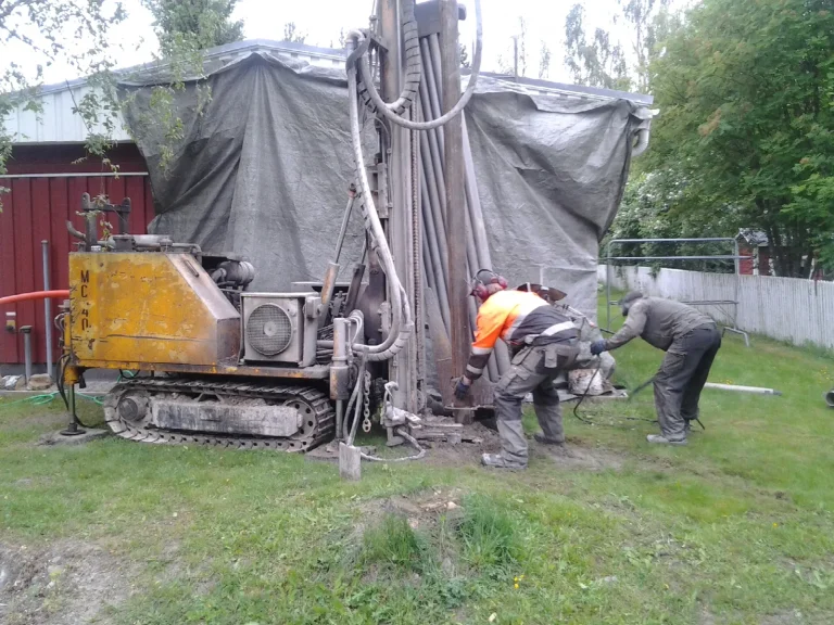Porauskone poraa lämpökaivoa omakotitalon pihalla, työmaa suojattu pressulla